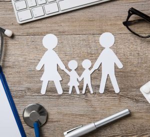 Top view of family paper chain on a doctor desk. Medical worktable with keyboard, blue stethoscope, pills and eyeglasses. Family healthcare, medicine and insurance concept.